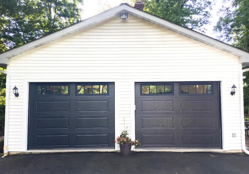 Two black long-panel garage doors with window tops on a white detached garage