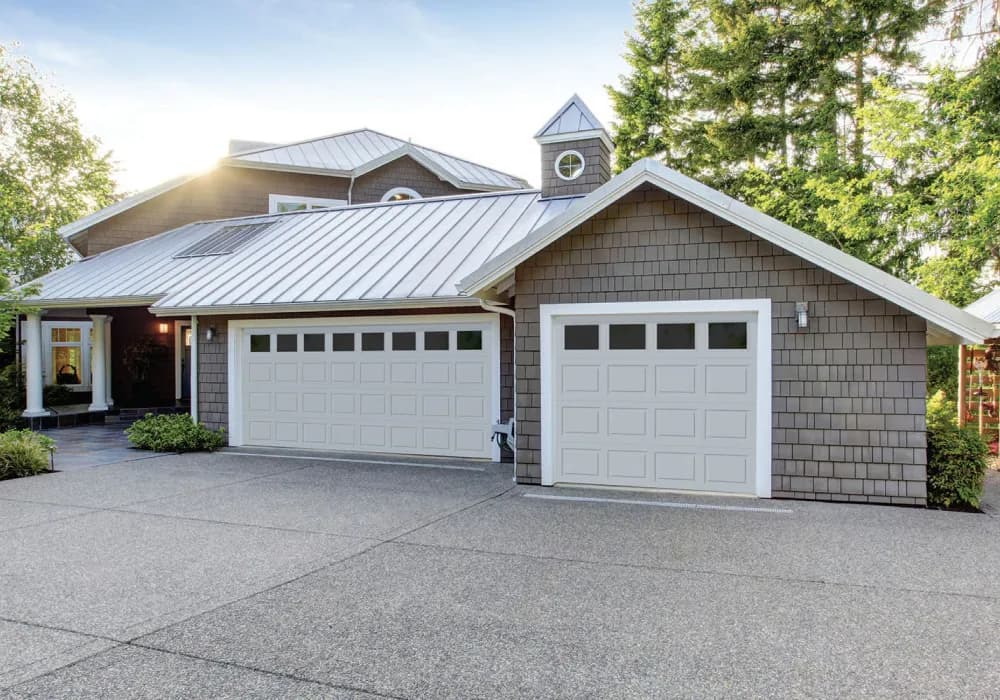 White short-panel garage doors with window tops on a home with a metal roof