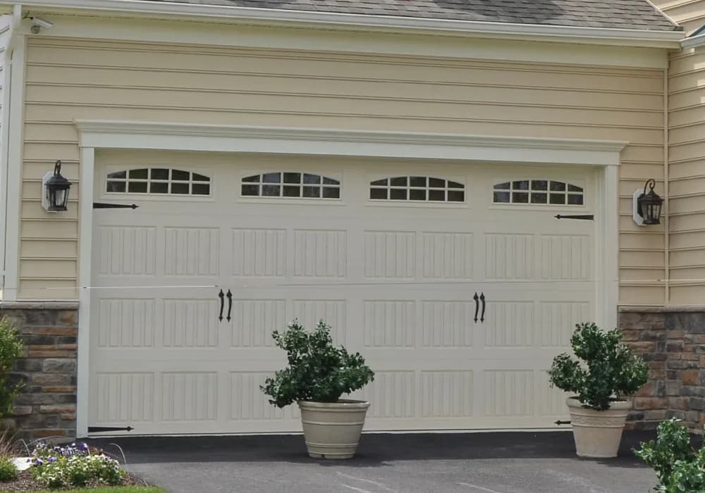 Cream carriage-style garage door with arched windows and decorative hardware