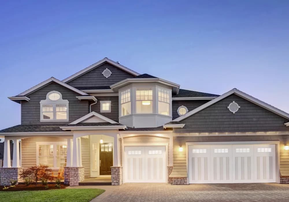 White carriage-style garage doors with window tops on a large home at dusk